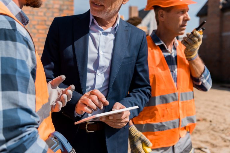 cropped view of constructor gesturing near co-worker and businessman with digital tablet